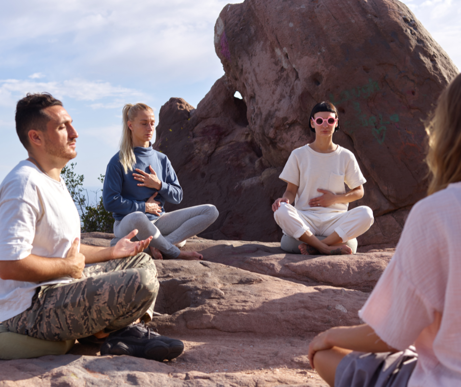 Personas meditando al aire libre en la naturaleza, practicando respiración consciente con las manos en el pecho y abdomen, una técnica vinculada a la longevidad, la reducción del estrés y la salud mental.