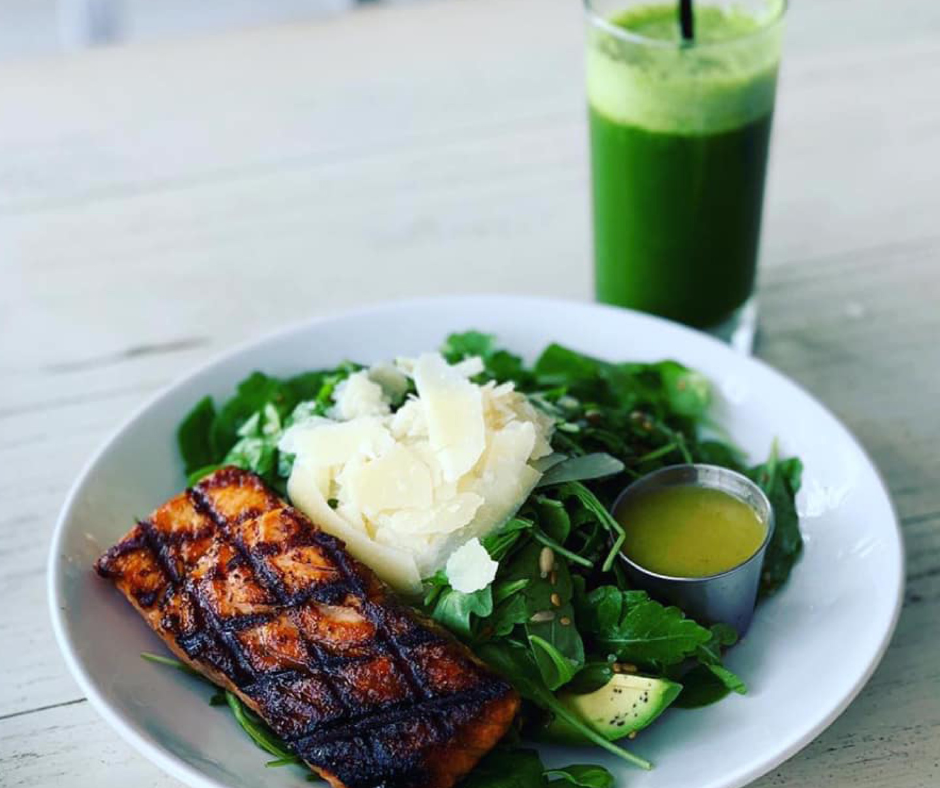Plato saludable con salmón a la parrilla, ensalada de hojas verdes, aguacate y queso, acompañado de jugo verde: ejemplo de dieta nutritiva inspirada en las Zonas Azules.