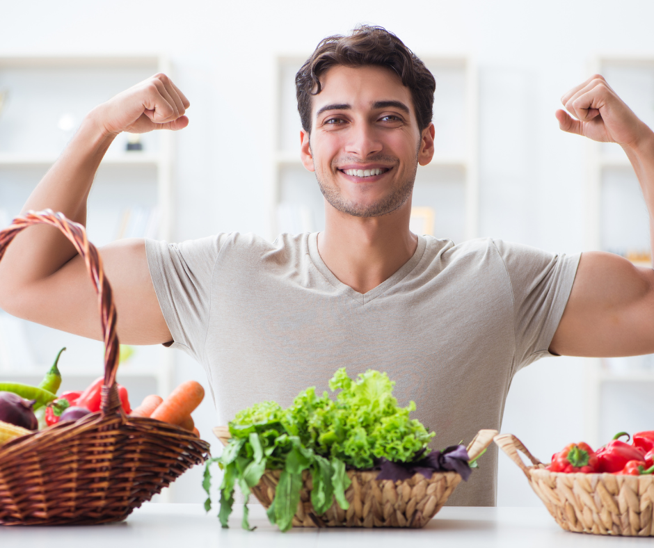 Hombre joven y saludable mostrando sus músculos mientras come alimentos frescos y vegetales para una dieta equilibrada.

