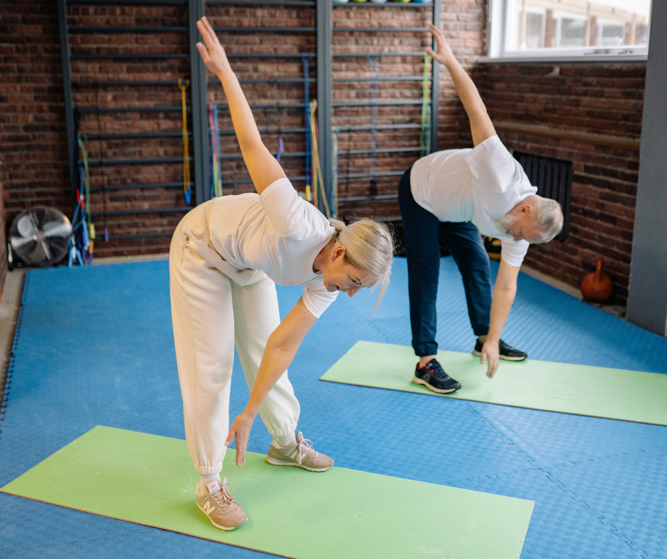 Adultos mayores haciendo ejercicios de estiramiento en colchonetas dentro de un gimnasio