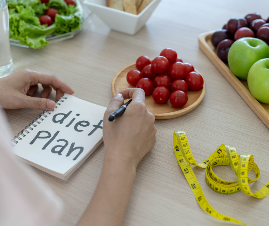 Persona planificando dieta saludable con cuaderno, frutas frescas y cinta métrica para control de peso.