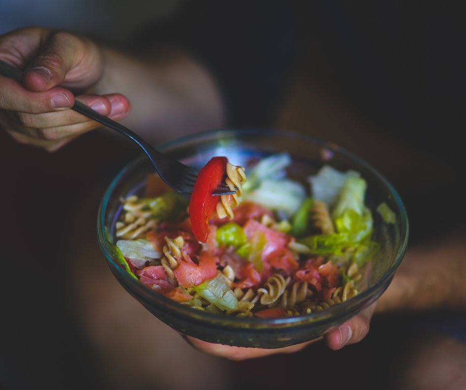 Ensalada saludable con pasta integral, lechuga y tomate en un bowl de vidrio.