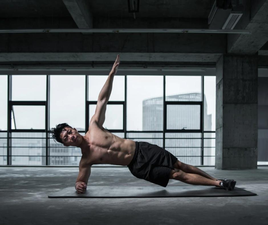 Hombre haciendo plancha lateral en un gimnasio moderno con grandes ventanales, destacando fuerza y entrenamiento corporal.