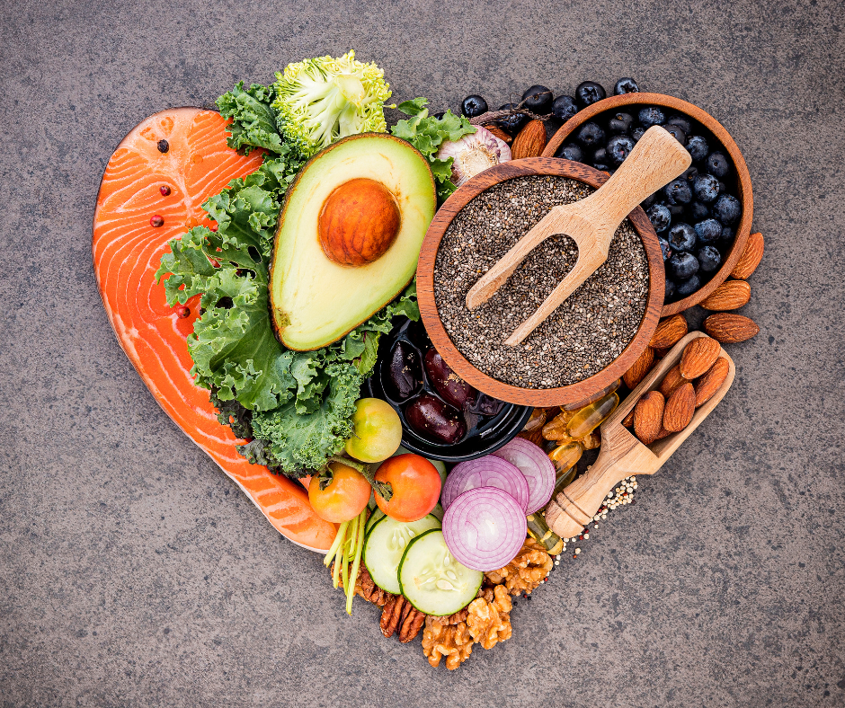 Alimentos saludables en forma de corazón, incluyendo salmón, palta, vegetales, frutas, semillas y frutos secos, representando una dieta equilibrada y beneficiosa para la salud.