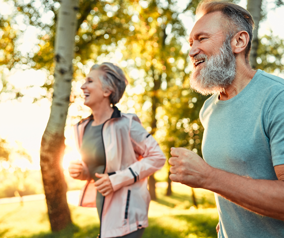 Pareja de adultos mayores corriendo al aire libre en un parque, disfrutando de la actividad física como herramienta para la longevidad y el envejecimiento saludable.