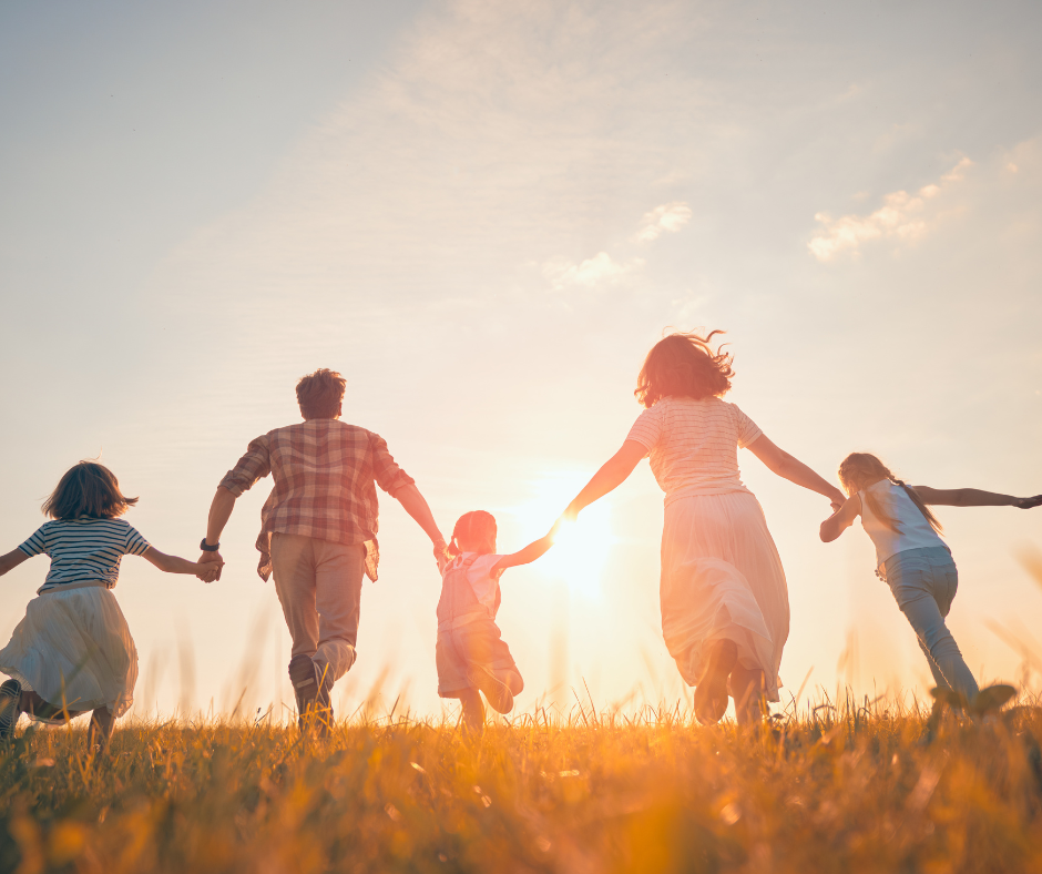 Familia corriendo junta en un campo al atardecer, simbolizando bienestar, energía y un ritmo cardíaco saludable en reposo.