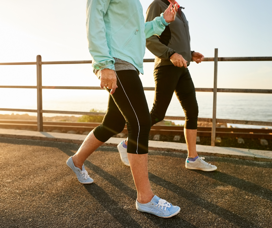 Dos personas caminando al aire libre junto al mar al amanecer, usando ropa deportiva, como símbolo de actividad física y bienestar.