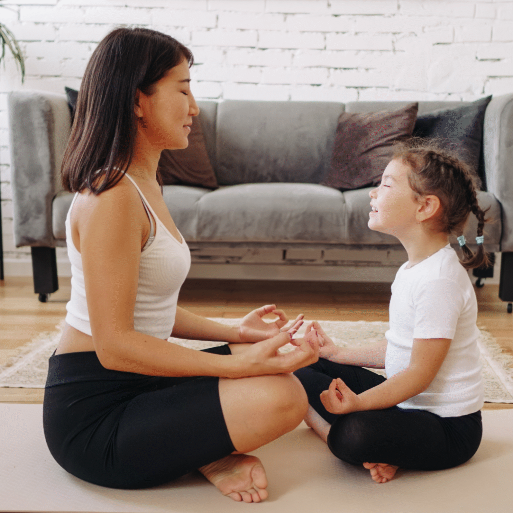 Madre e hija meditando juntas en casa, sentadas en postura de loto sobre una esterilla, practicando mindfulness y conexión familiar para el bienestar.