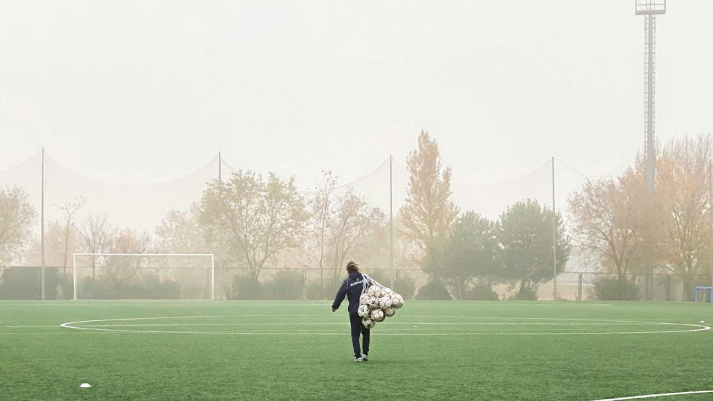 Entrenador de fútbol caminando en una cancha con pelotas, representando el trabajo de resistencia, condición física y entrenamiento cardiovascular específico para futbolistas.